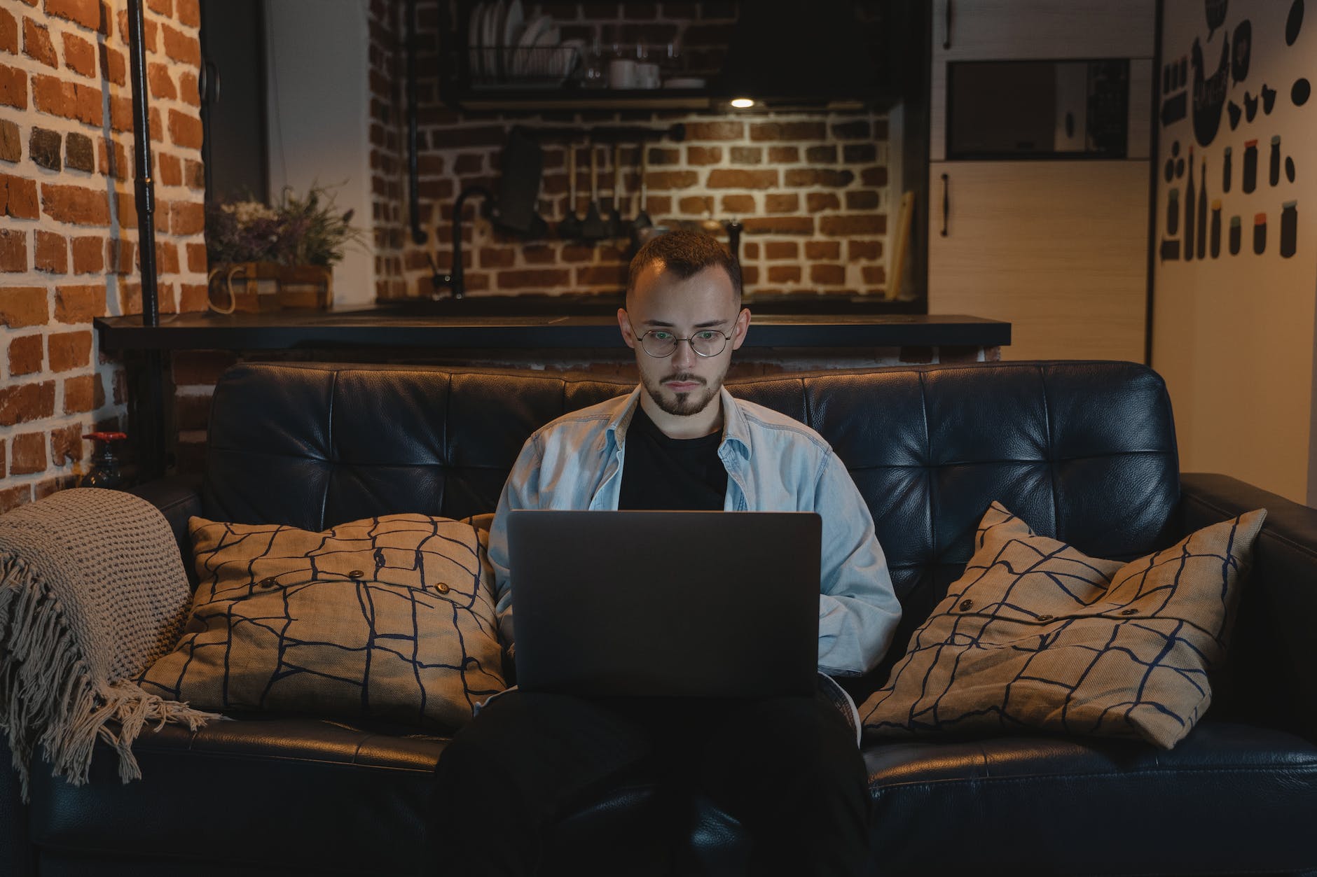 man in black crew neck t shirt and denim jacket sitting on a couch using his laptop